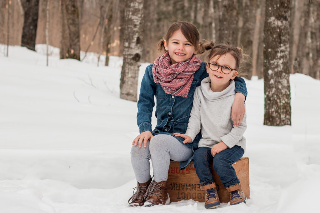 2 girls sitting on a crate in a winter forest